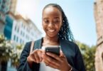 A woman looking and smiling at her phone as she scrolls through her feed.