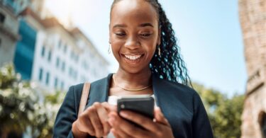 A woman looking and smiling at her phone as she scrolls through her feed.
