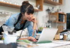 Business owner of a cafe leaning over the counter and looking at a laptop.
