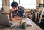 Tired woodworker working on a laptop in his carpentry studio
