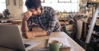 Tired woodworker working on a laptop in his carpentry studio